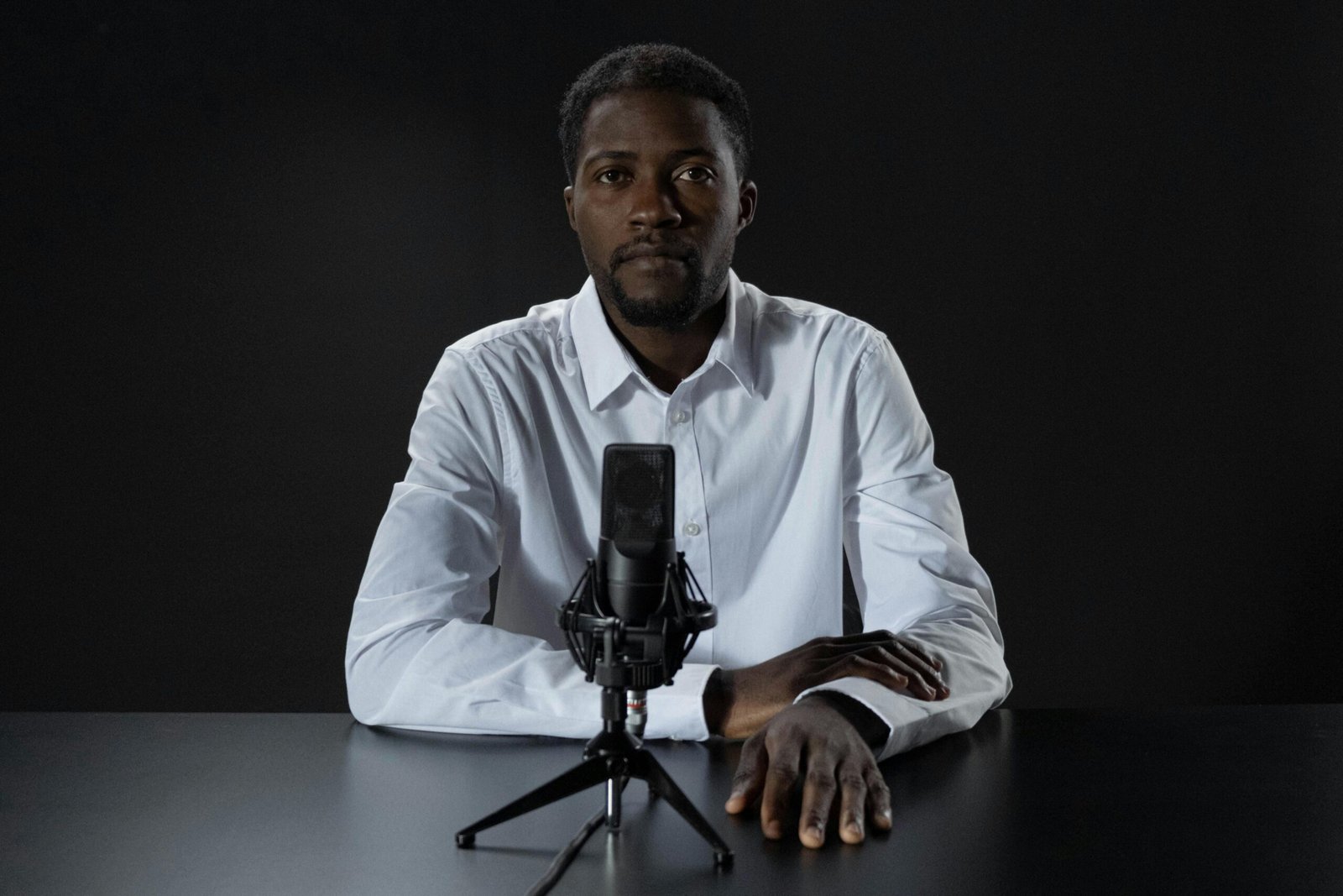 Serious African American man sitting at a table with a microphone, ready to podcast or record.